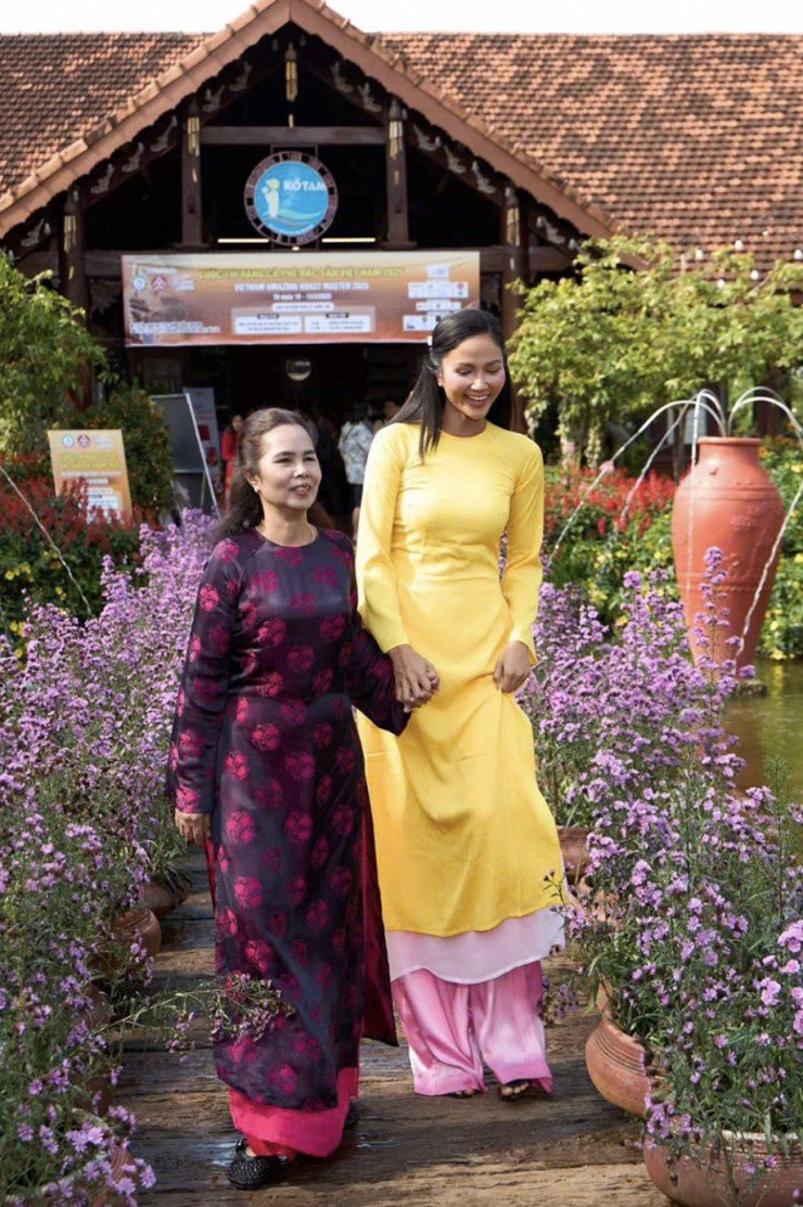 Hoa hậu mặc áo dài của nhà thiết kế Thủy Nguyễn, tạo dáng xì tin, thoải mái trong khi mẹ cô tỏ ra bẽn lẽn, ngại ngùng trước ống kính. Bà H'Ngơn Niê không biết tiếng Kinh, chủ yếu ở nhà làm việc nương rẫy, ít khi ra ngoài.