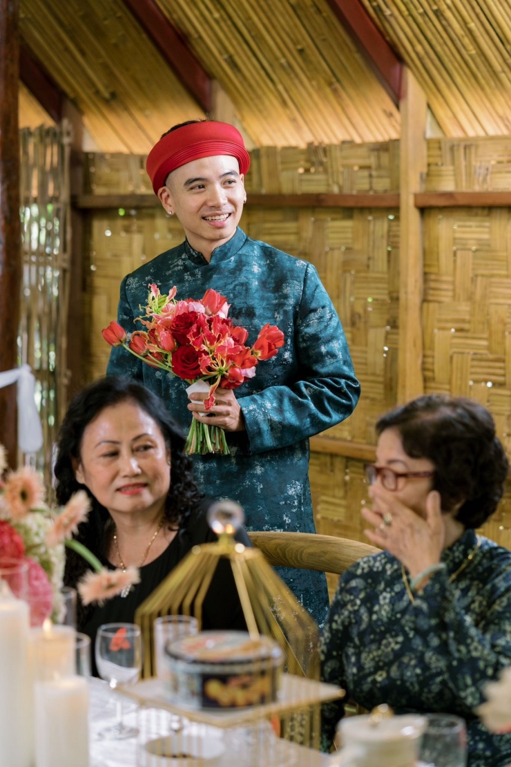 Chú rể Tuấn Khôi mặc áo dài khăn đóng, chào họ nhà gái. Nhiếp ảnh gia cầm bó hoa cưới được kết từ hoa hồng đỏ.