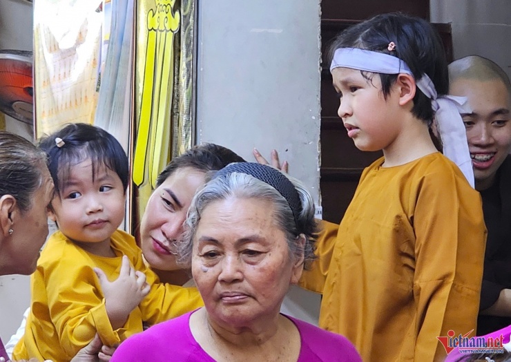 Con trai riêng của Ngọc Tiền (phải) chăm sóc, trông coi em trai để mẹ và người lớn tiếp đón khách. Con gái của Ngọc Tiền cũng phụ mẹ đón khách, làm lễ.