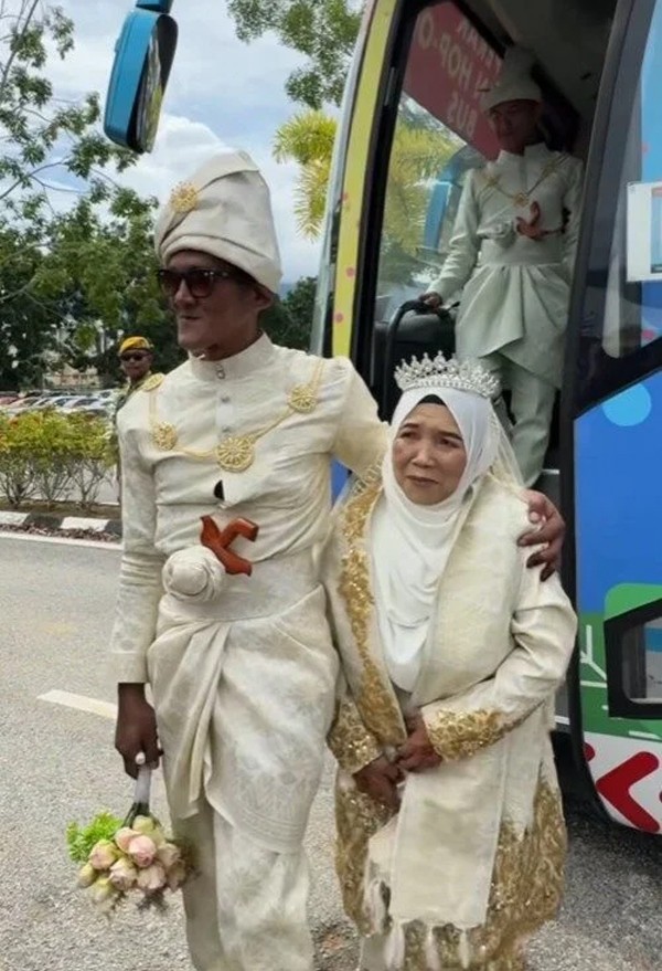 Chú rể Nizam khoác vai cô dâu 70 tuổi đến nơi tổ chức đám cưới tập thể. Ảnh: FB