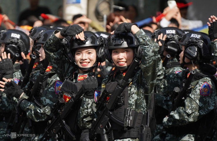 Trên đường di chuyển tới điểm tập kết ở cung Quần Ngựa, do vẫn phải đứng trong hàng lối, cách xa với người dân, nữ cảnh sát đặc nhiệm Bộ Công an vẫn có cách thể hiện tình cảm. Ảnh: Lưu Quý